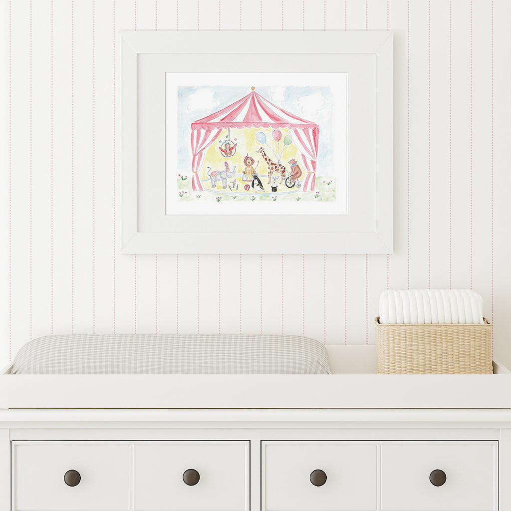 Framed children's illustration of a circus scene on a white wall above a white dresser.