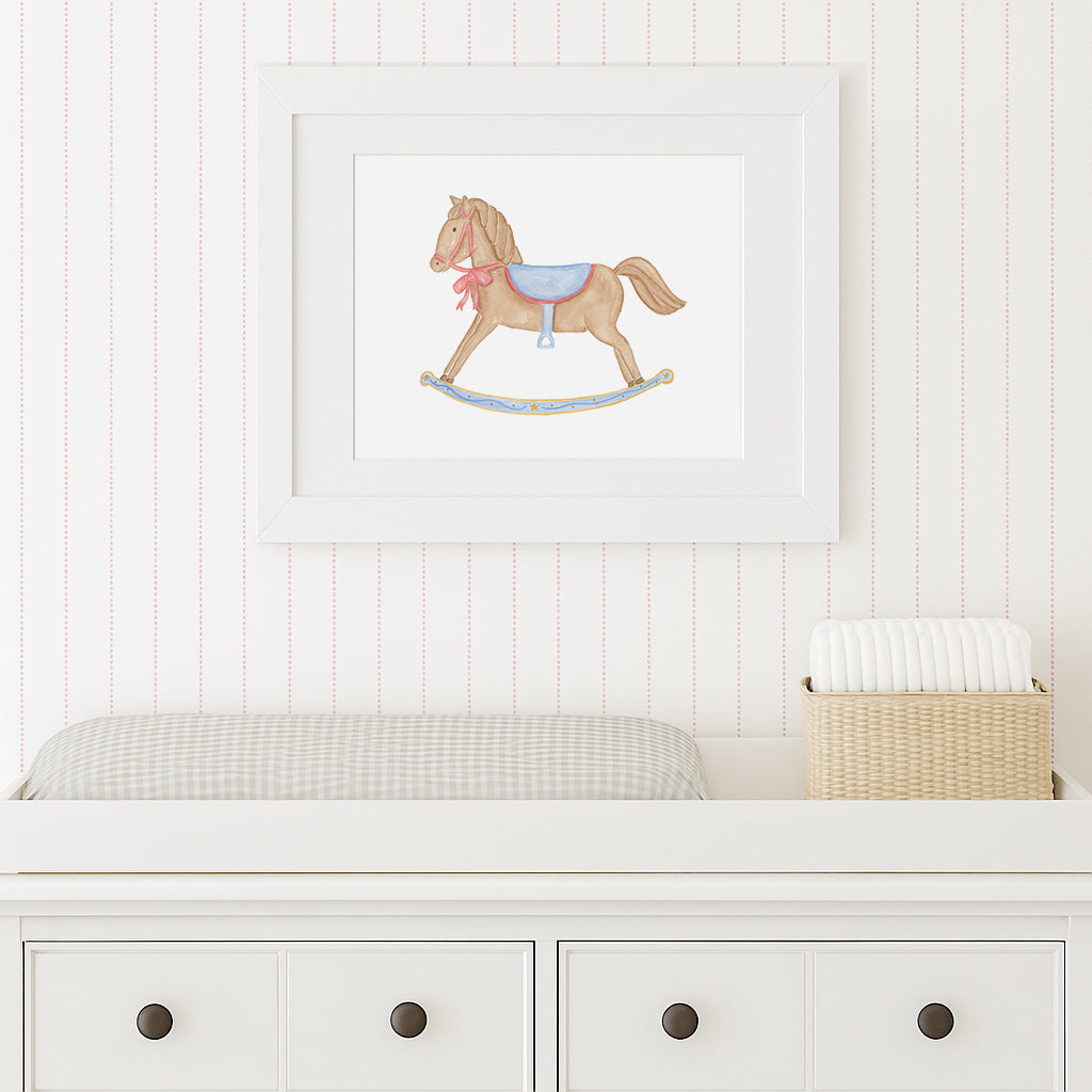 Framed illustration of a rocking horse on a wall above a white dresser.